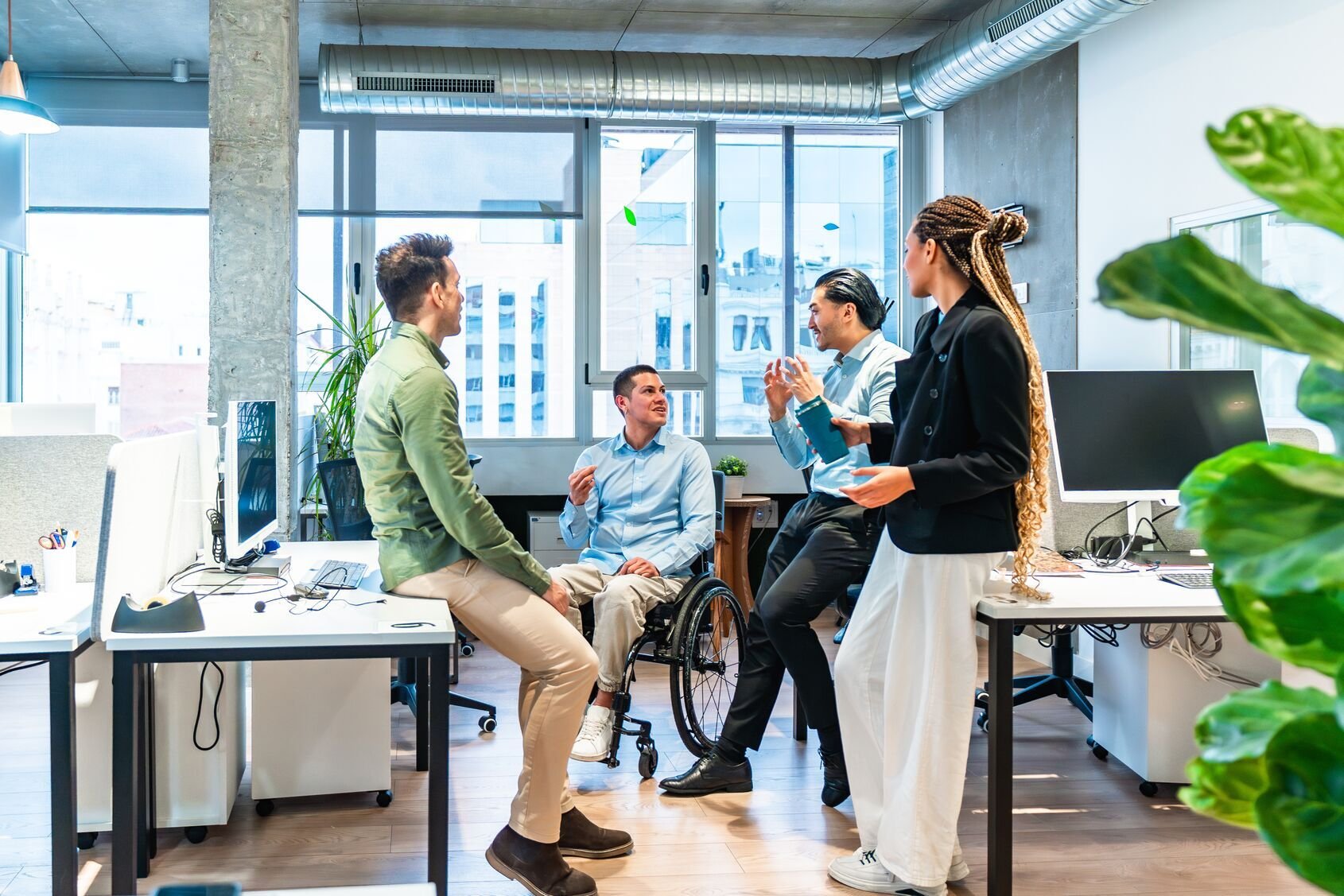 Web_Wide-Diverse business team discussing project in modern office with disabled colleague in wheelchair